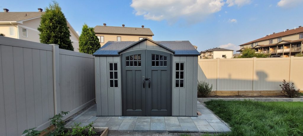 Grey Plastic Shed Shaped like a Tiny House on A Stone Patio